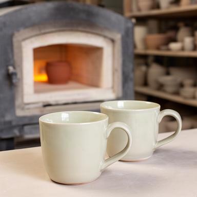Due tazze in ceramica fatte a mano con smalto chiaro vicino a un forno dello studio
