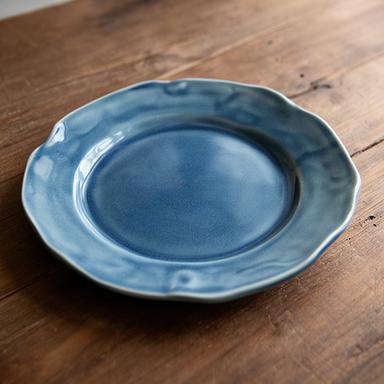 Piatto artigianale blu con bordo irregolare fotografato su un tavolo in legno